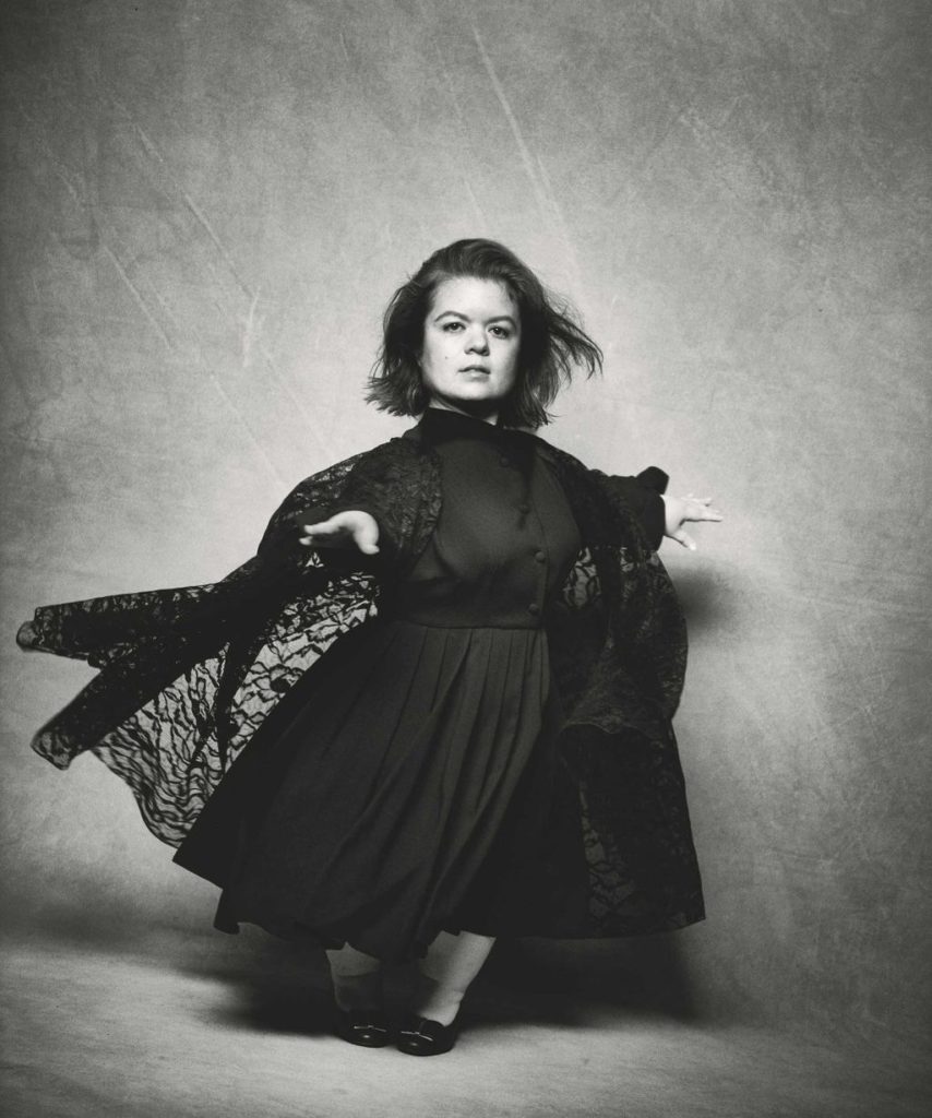 Sinéad Burke photographiée par Peter Lindbergh pose pour Vogue dans une magnifique robe noir. Elle est très élégante.